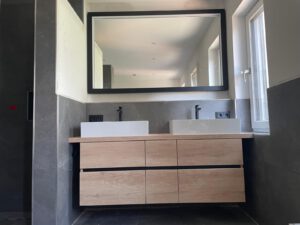 Waschtisch zwischen den Wänden und Spiegel mit LED Beleuchtung auf schwarzer Holzplatte