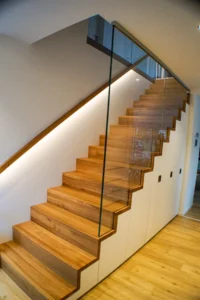 Treppenschrank unter Faltwerktreppe mit eingenutetem Glasgeländer und beleuchtetem Handlauf